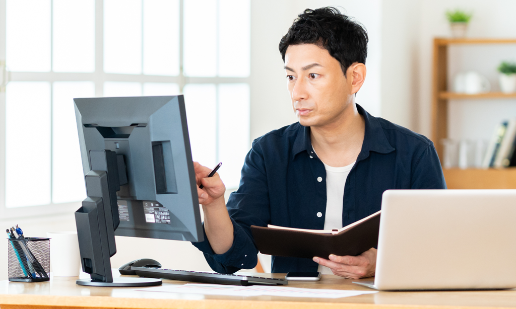 デスクトップパソコンのモニターを凝視する男性画像